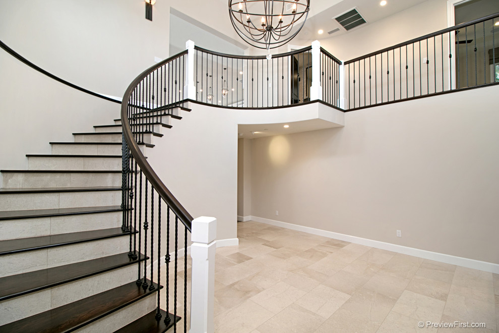 This is an example of a large beach style wood spiral staircase in Orange County with marble risers and metal railing.