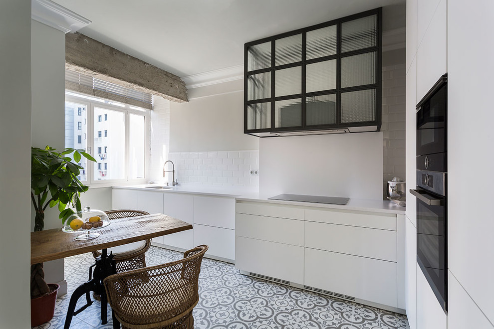 Photo of a mid-sized transitional single-wall eat-in kitchen in Other with an undermount sink, flat-panel cabinets, white cabinets, white splashback, black appliances, ceramic floors, no island, multi-coloured floor and subway tile splashback.