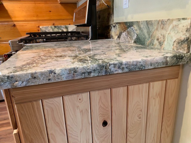 Open concept kitchen - mid-sized rustic medium tone wood floor and brown floor open concept kitchen idea with an undermount sink, flat-panel cabinets, light wood cabinets, granite countertops, gray backsplash, stone slab backsplash, stainless steel appliances and gray countertops