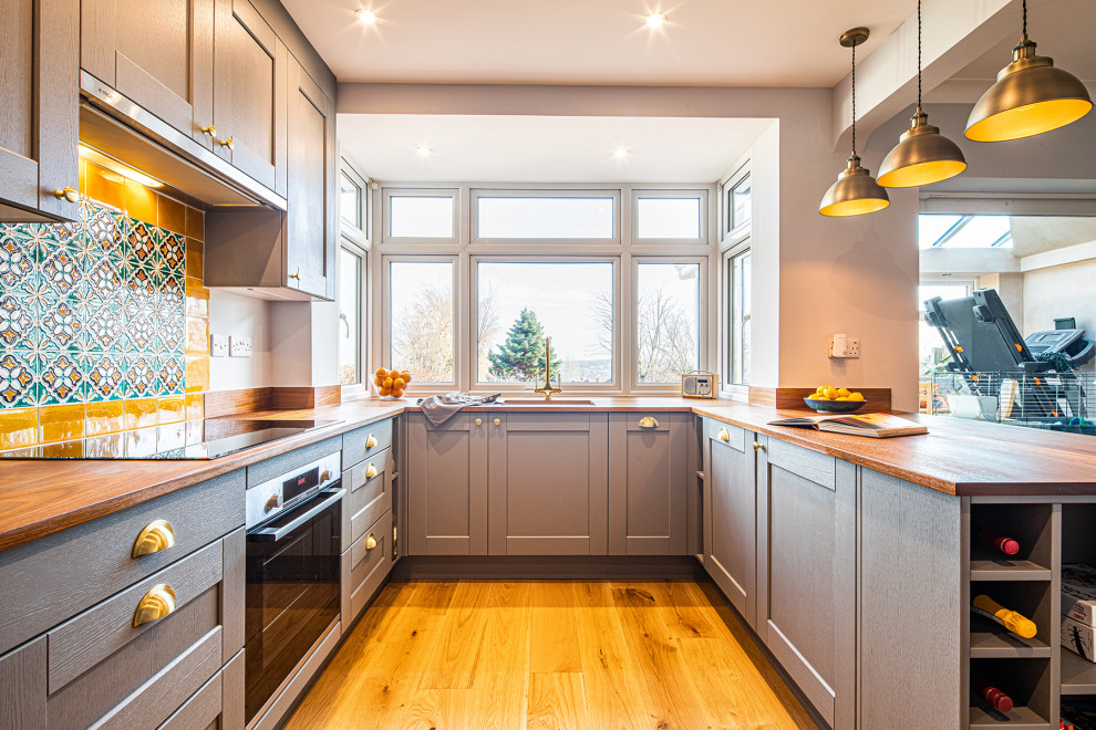 Photo of a mid-sized transitional u-shaped eat-in kitchen in Other with an undermount sink, shaker cabinets, grey cabinets, wood benchtops, yellow splashback, terra-cotta splashback, a peninsula, brown floor and brown benchtop.