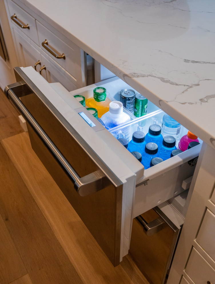 Large transitional u-shaped light wood floor kitchen photo with an undermount sink, shaker cabinets, white cabinets, quartz countertops, white backsplash, marble backsplash, paneled appliances, two islands and white countertops