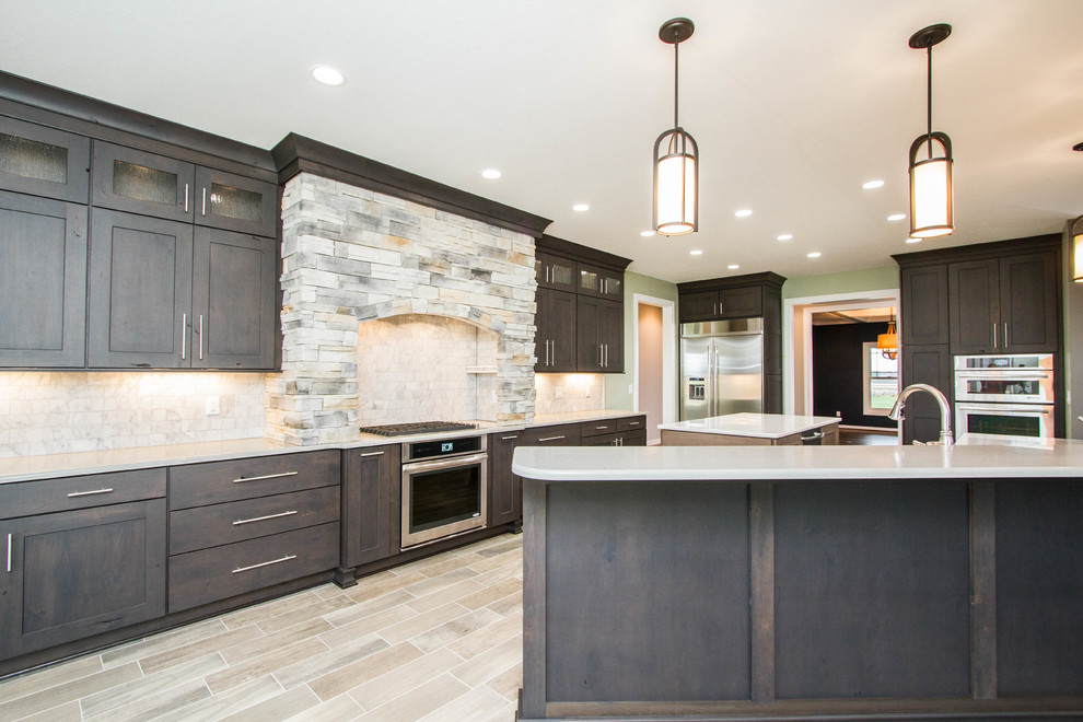 Open concept kitchen - transitional l-shaped porcelain tile and beige floor open concept kitchen idea with a farmhouse sink, raised-panel cabinets, dark wood cabinets, quartzite countertops, black backsplash, stainless steel appliances and two islands