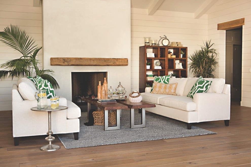 Inspiration for a mid-sized tropical enclosed living room in Los Angeles with white walls, medium hardwood floors, a standard fireplace, no tv and a plaster fireplace surround.