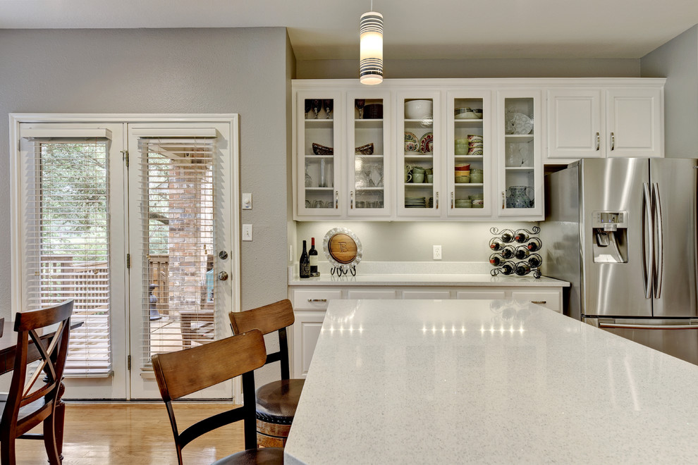 Design ideas for a mid-sized transitional u-shaped eat-in kitchen in Austin with an undermount sink, white cabinets, quartz benchtops, white splashback, stone slab splashback, stainless steel appliances, light hardwood floors, a peninsula and raised-panel cabinets.