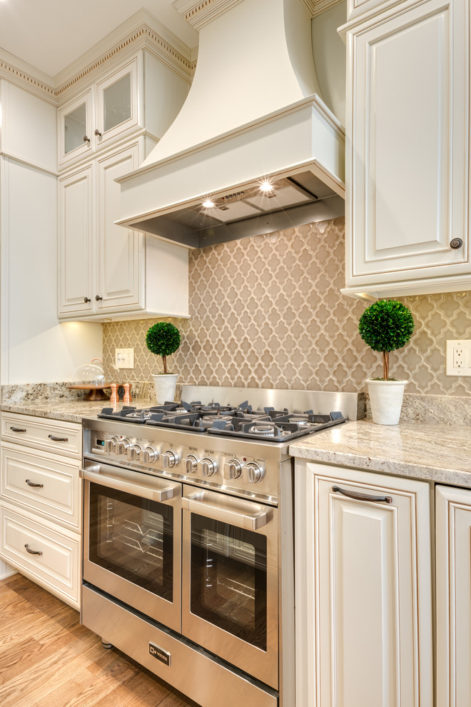 This is an example of a mid-sized traditional u-shaped eat-in kitchen in Atlanta with an undermount sink, raised-panel cabinets, white cabinets, granite benchtops, beige splashback, stainless steel appliances, light hardwood floors, with island, porcelain splashback, brown floor and beige benchtop.