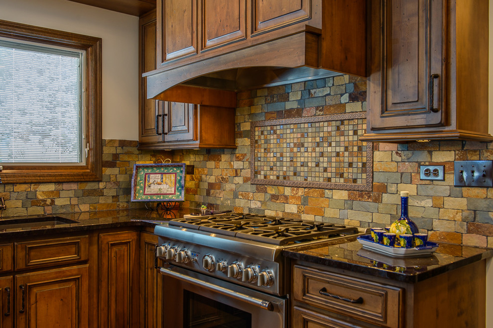 Example of a large mountain style kitchen design in Chicago with an undermount sink, raised-panel cabinets, granite countertops, stone tile backsplash, stainless steel appliances and an island