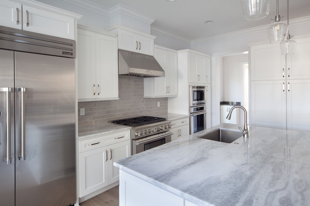 Large modern galley open plan kitchen in Orlando with a drop-in sink, flat-panel cabinets, white cabinets, granite benchtops, grey splashback, subway tile splashback, stainless steel appliances, light hardwood floors and multiple islands.