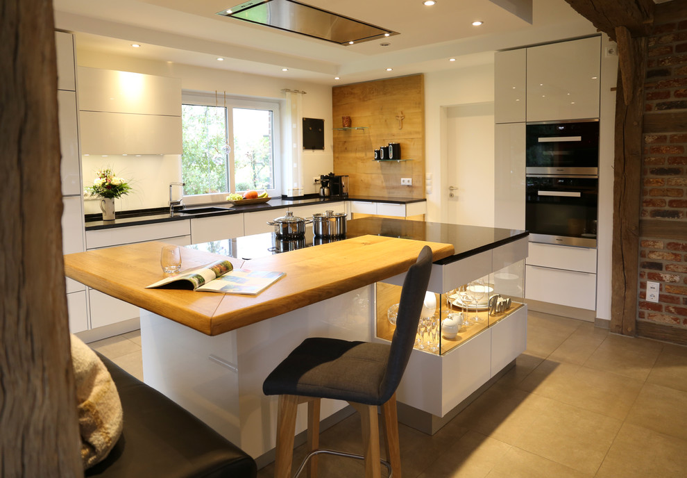 This is an example of a large contemporary l-shaped open plan kitchen in Bremen with an integrated sink, flat-panel cabinets, white cabinets, granite benchtops, white splashback, glass sheet splashback, stainless steel appliances, marble floors, multiple islands and beige floor.