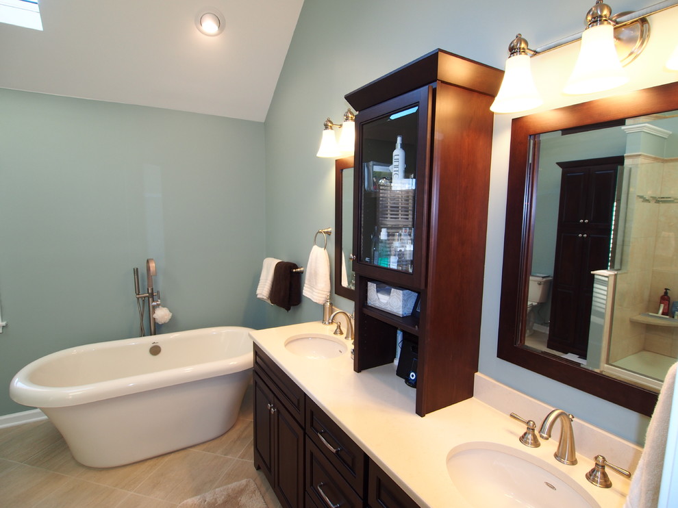 Photo of a large transitional bathroom in New York with an undermount sink, raised-panel cabinets, dark wood cabinets, engineered quartz benchtops, a freestanding tub, a double shower, a one-piece toilet, beige tile, porcelain tile, blue walls and limestone floors.