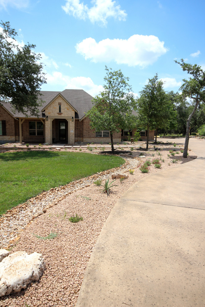 This is an example of a large front driveway full sun garden in Austin with decorative stones and lawn edging.