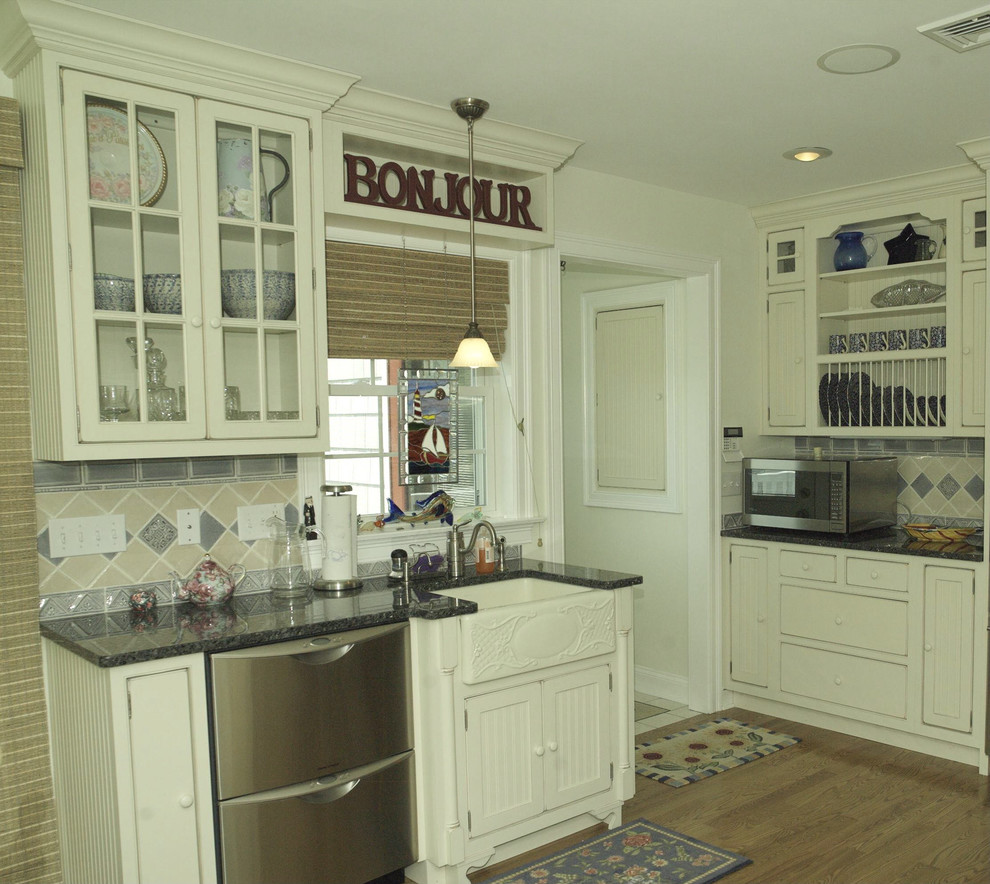 This is an example of a small beach style u-shaped eat-in kitchen in Providence with beaded inset cabinets, white cabinets, granite benchtops, blue splashback, light hardwood floors, no island, a farmhouse sink, ceramic splashback and stainless steel appliances.