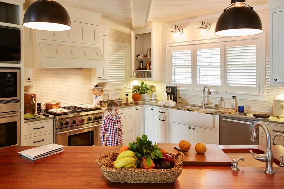 Mid-sized transitional l-shaped enclosed kitchen photo in Minneapolis with a farmhouse sink, recessed-panel cabinets, white cabinets, white backsplash, subway tile backsplash, stainless steel appliances, an island and wood countertops