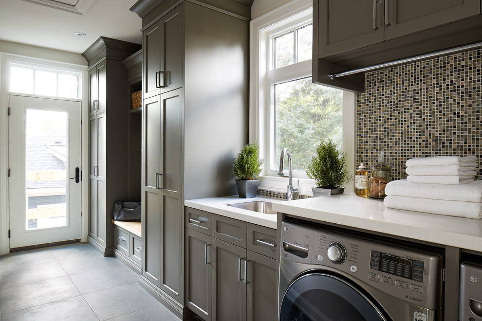 Large contemporary single-wall utility room in Toronto with an undermount sink, shaker cabinets, grey cabinets, quartz benchtops, grey walls, porcelain floors and a side-by-side washer and dryer.