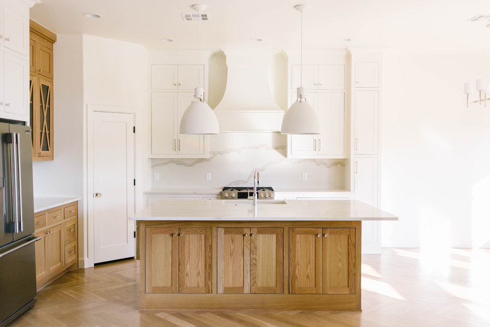 Design ideas for a transitional l-shaped kitchen in Oklahoma City with an undermount sink, shaker cabinets, medium wood cabinets, white splashback, stone slab splashback, stainless steel appliances, medium hardwood floors, with island, brown floor and white benchtop.
