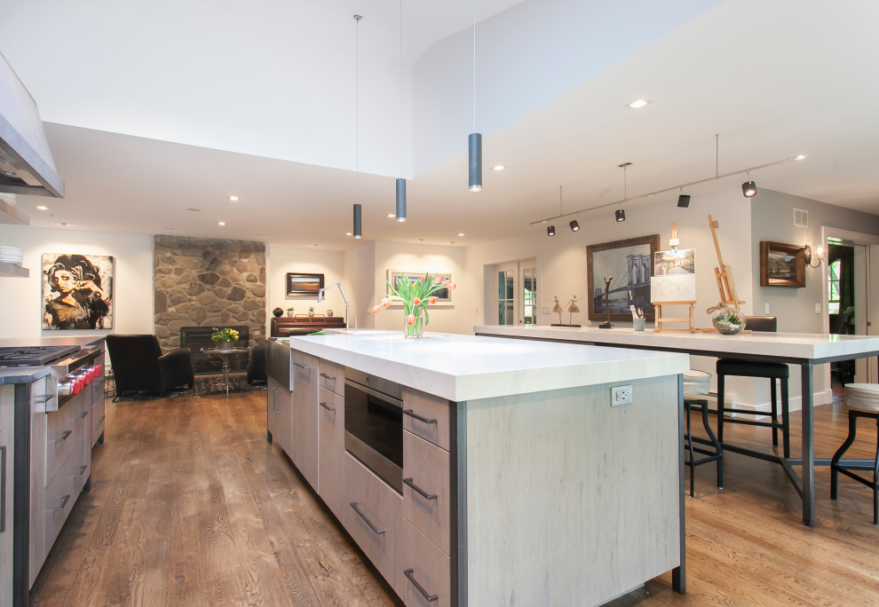 Inspiration for an expansive industrial single-wall eat-in kitchen in Bridgeport with a single-bowl sink, flat-panel cabinets, grey cabinets, quartz benchtops, brown splashback, travertine splashback, stainless steel appliances, light hardwood floors, multiple islands, brown floor and white benchtop.
