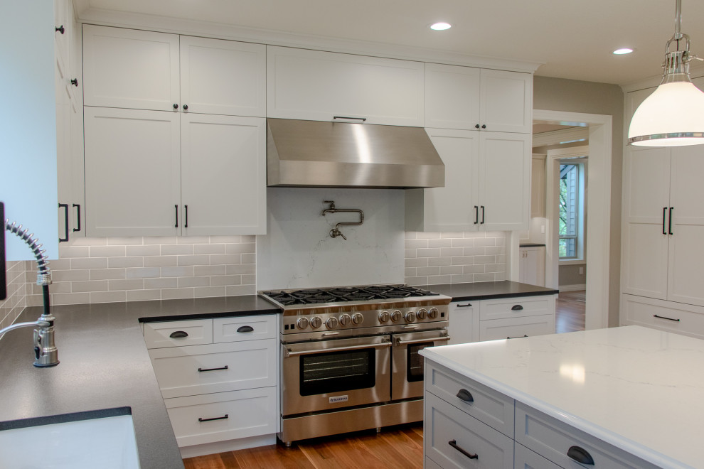 Inspiration for a transitional l-shaped medium tone wood floor and brown floor kitchen remodel in Portland with an undermount sink, shaker cabinets, white cabinets, gray backsplash, subway tile backsplash, paneled appliances, an island and black countertops