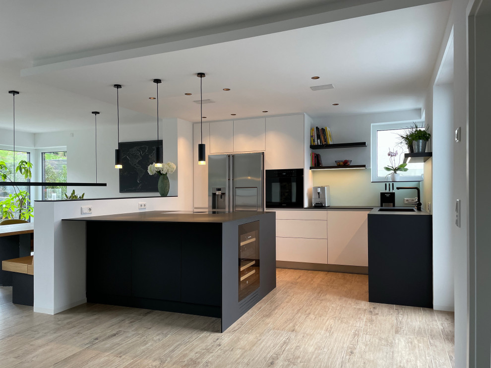 Photo of a large contemporary open plan kitchen in Cologne with ceramic flooring, beige floors, a submerged sink, flat-panel cabinets, white cabinets, laminate countertops, green splashback, glass sheet splashback, stainless steel appliances, a breakfast bar and black worktops.