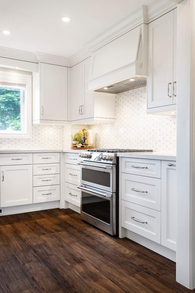 Inspiration for a large transitional u-shaped dark wood floor and brown floor eat-in kitchen remodel in Toronto with an undermount sink, recessed-panel cabinets, white cabinets, quartz countertops, white backsplash, ceramic backsplash, stainless steel appliances, an island and white countertops
