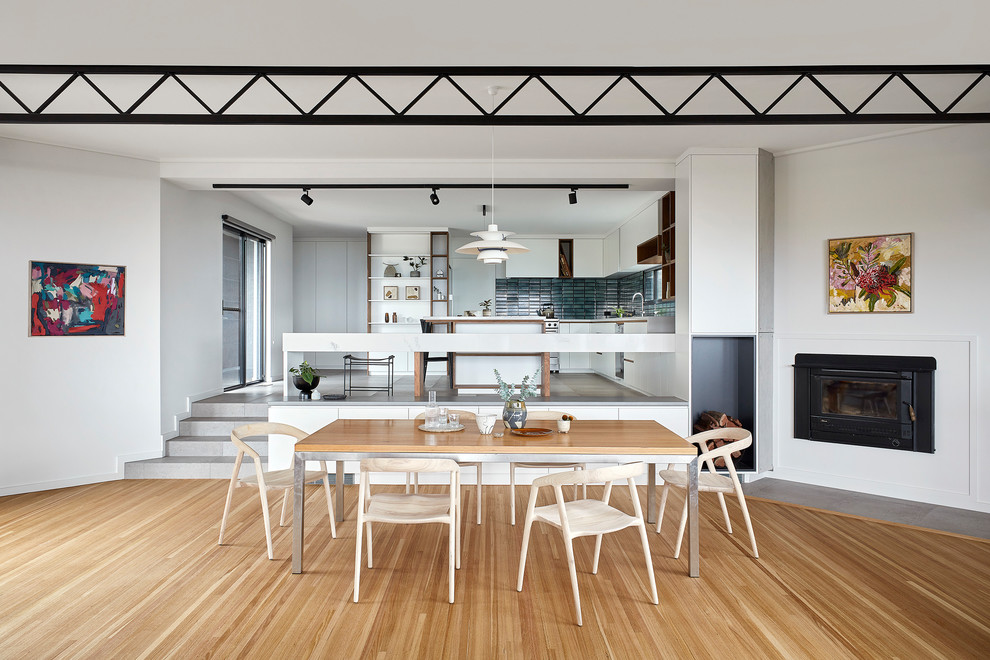 Design ideas for a mid-sized contemporary kitchen/dining combo in Melbourne with white walls, light hardwood floors, a wood stove, brown floor, a tile fireplace surround and exposed beam.