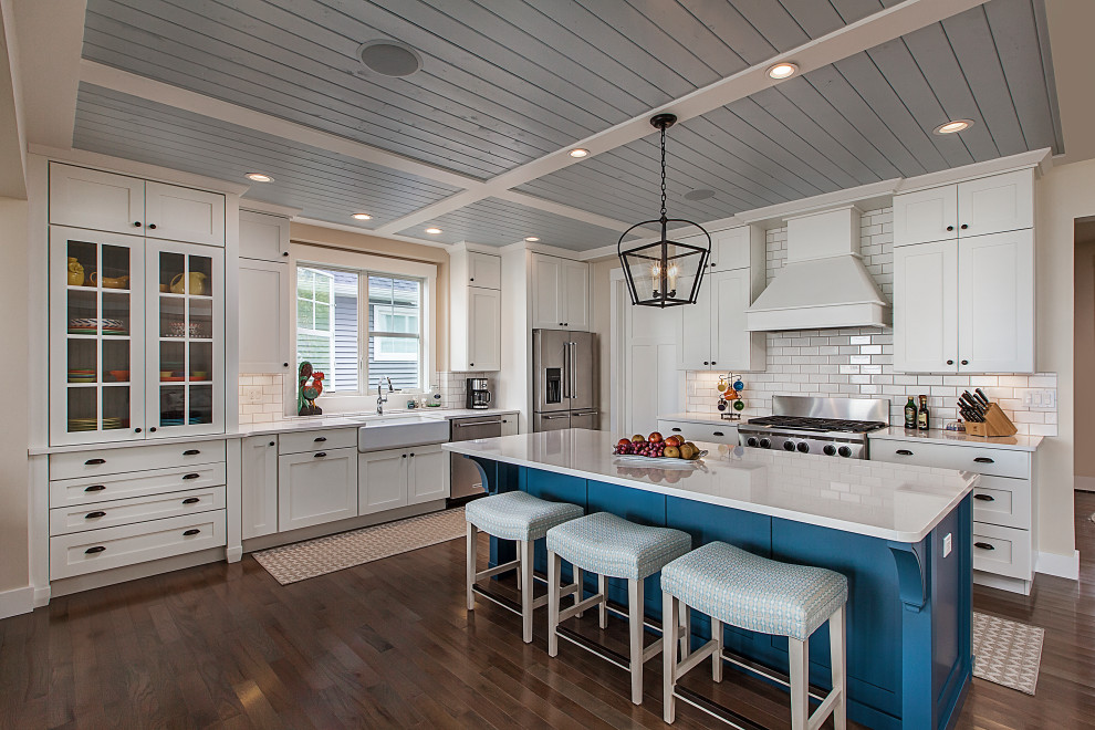 Large beach style l-shaped kitchen in Grand Rapids with a farmhouse sink, white cabinets, quartzite benchtops, white splashback, subway tile splashback, stainless steel appliances, with island, white benchtop, shaker cabinets, dark hardwood floors, brown floor and timber.