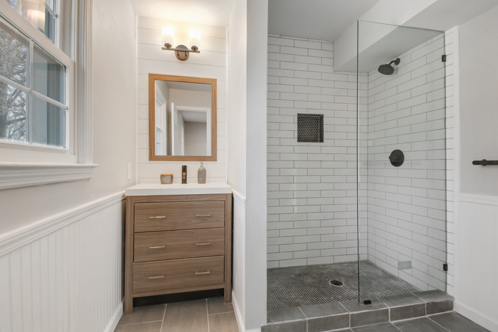 Photo of a mid-sized country 3/4 bathroom in Kansas City with recessed-panel cabinets, light wood cabinets, an open shower, white tile, subway tile, grey walls, cement tiles, quartzite benchtops, grey floor, white benchtops, a single vanity, a freestanding vanity and panelled walls.