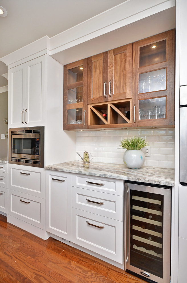 Imagen de cocina comedor clásica renovada de tamaño medio con fregadero de doble seno, armarios estilo shaker, puertas de armario blancas, encimera de granito, salpicadero blanco, salpicadero de azulejos de cerámica, electrodomésticos de acero inoxidable, suelo de madera en tonos medios y una isla