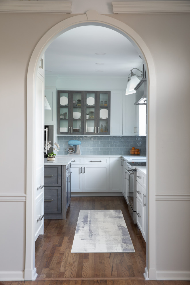 Mid-sized transitional l-shaped medium tone wood floor and brown floor enclosed kitchen photo with an undermount sink, shaker cabinets, white cabinets, quartz countertops, blue backsplash, subway tile backsplash, stainless steel appliances, an island and white countertops