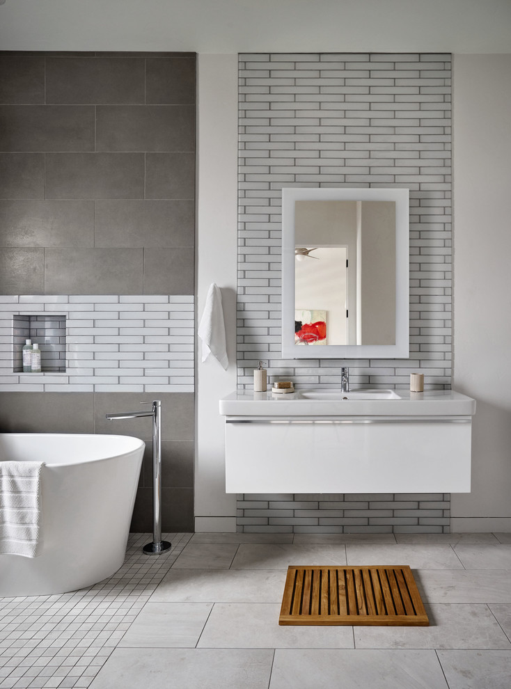 Photo of an expansive contemporary master bathroom in Portland with flat-panel cabinets, white cabinets, a freestanding tub, glass tile, multi-coloured walls, porcelain floors, a wall-mount sink, solid surface benchtops and white tile.