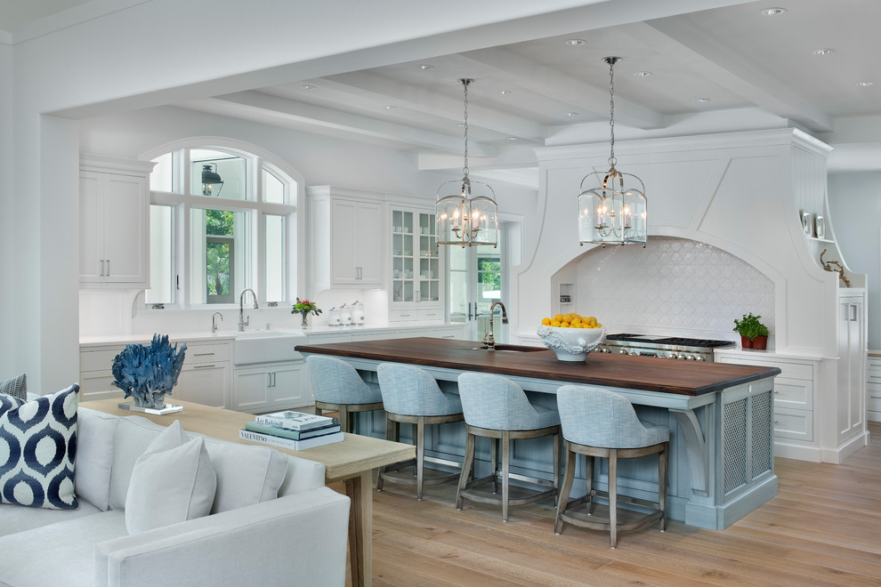 Inspiration for a mid-sized coastal beige floor and medium tone wood floor open concept kitchen remodel with a farmhouse sink, white cabinets, white backsplash, stainless steel appliances, an island, white countertops and recessed-panel cabinets