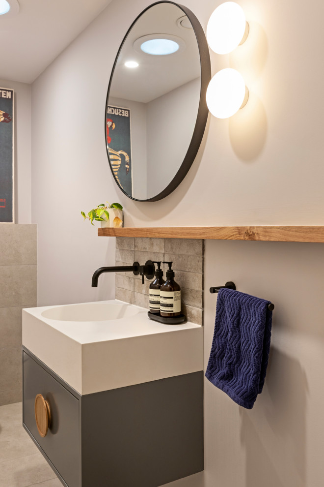 Photo of a small contemporary powder room in Melbourne with recessed-panel cabinets, blue cabinets, a wall-mount toilet, gray tile, ceramic tile, grey walls, porcelain floors, an integrated sink, solid surface benchtops, grey floor, white benchtops and a floating vanity.