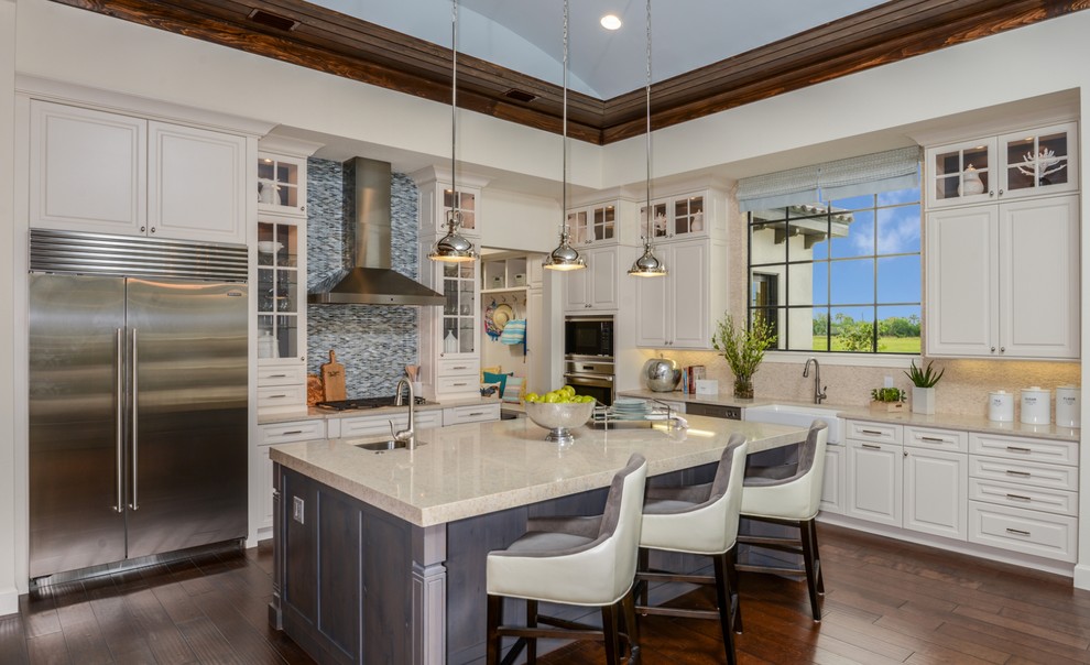 Example of a transitional l-shaped dark wood floor and brown floor kitchen design in Tampa with a farmhouse sink, raised-panel cabinets, white cabinets, quartzite countertops, beige backsplash, stainless steel appliances, an island and beige countertops