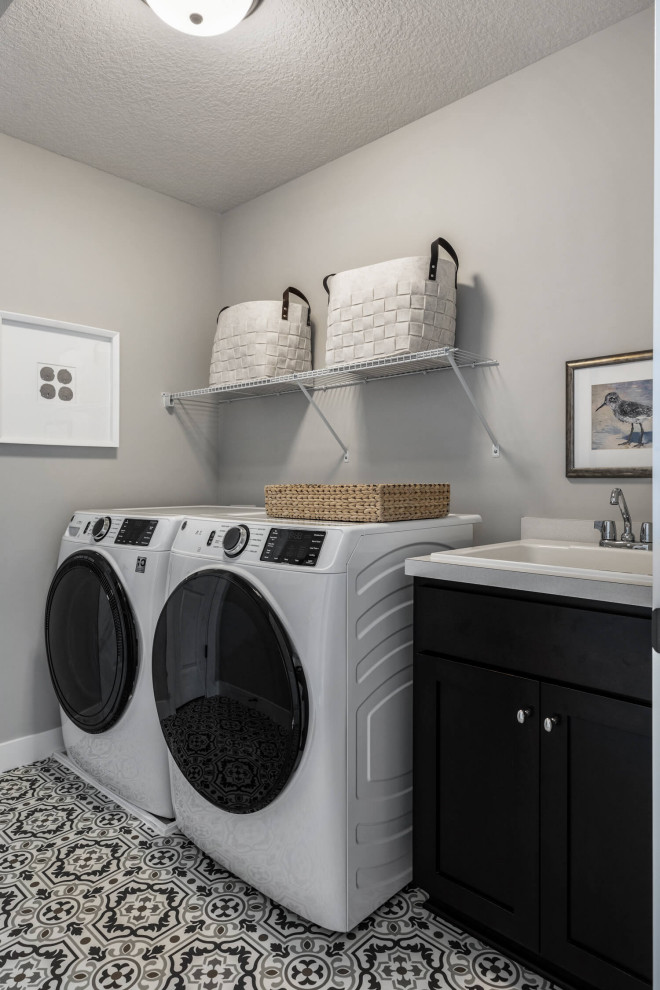 Esempio di una sala lavanderia chic con lavello a vasca singola, ante in stile shaker, ante in legno bruno, pareti grigie, pavimento in vinile, lavatrice e asciugatrice affiancate e pavimento nero