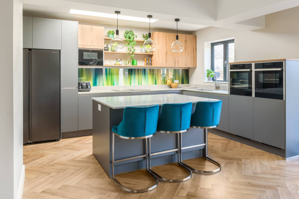 Inspiration for a medium sized contemporary l-shaped enclosed kitchen in Sussex with a built-in sink, flat-panel cabinets, grey cabinets, quartz worktops, multi-coloured splashback, black appliances, light hardwood flooring, an island, brown floors, white worktops, exposed beams and feature lighting.