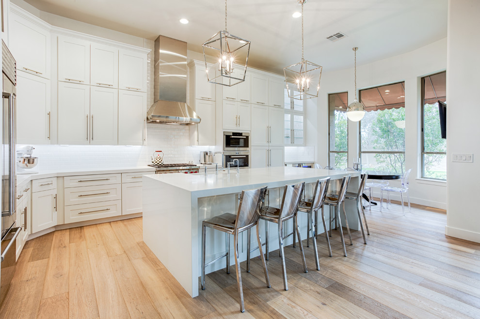 Large transitional l-shaped eat-in kitchen in Phoenix with shaker cabinets, white cabinets, quartz benchtops, white splashback, ceramic splashback, stainless steel appliances, light hardwood floors, with island and a farmhouse sink.