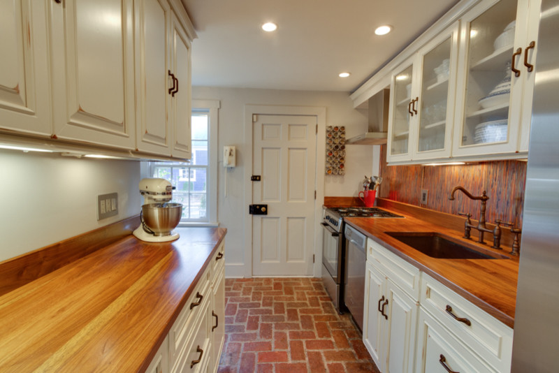 Small transitional galley separate kitchen in DC Metro with a single-bowl sink, recessed-panel cabinets, beige cabinets, wood benchtops, multi-coloured splashback, stainless steel appliances, brick floors and no island.