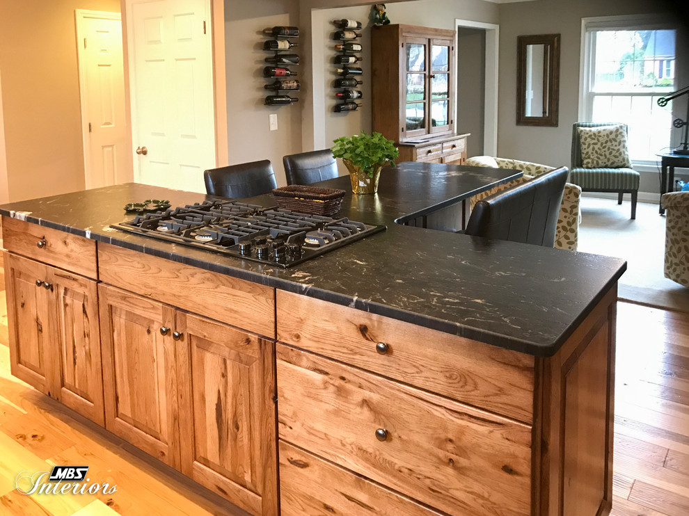 Large mountain style l-shaped light wood floor and beige floor eat-in kitchen photo with an undermount sink, raised-panel cabinets, medium tone wood cabinets, granite countertops, gray backsplash, ceramic backsplash, stainless steel appliances and an island