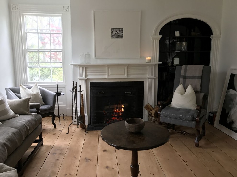Photo of a mid-sized scandinavian formal enclosed living room in New York with white walls, light hardwood floors, a standard fireplace, a wood fireplace surround, no tv and brown floor.