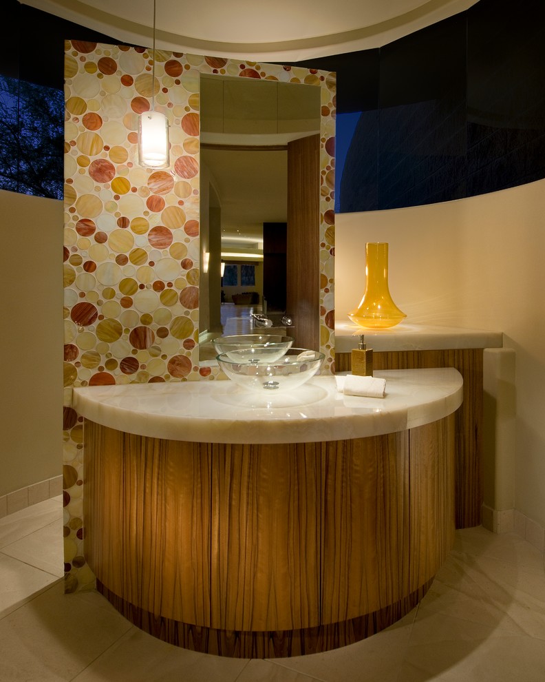 Photo of a small contemporary powder room in Phoenix with a vessel sink, flat-panel cabinets, medium wood cabinets, onyx benchtops, a one-piece toilet, orange tile, glass tile, white walls and limestone floors.