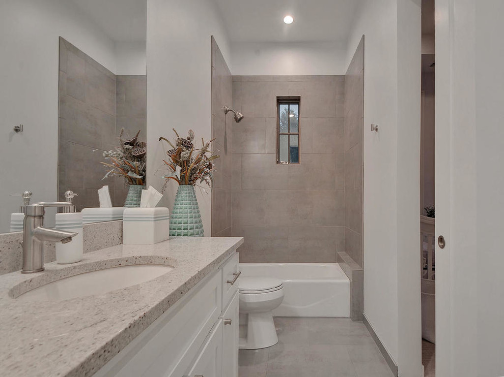 Inspiration for a mid-sized contemporary kids bathroom in Austin with shaker cabinets, white cabinets, an alcove tub, a shower/bathtub combo, a one-piece toilet, gray tile, ceramic tile, white walls, ceramic floors, an undermount sink, engineered quartz benchtops, grey floor and a shower curtain.