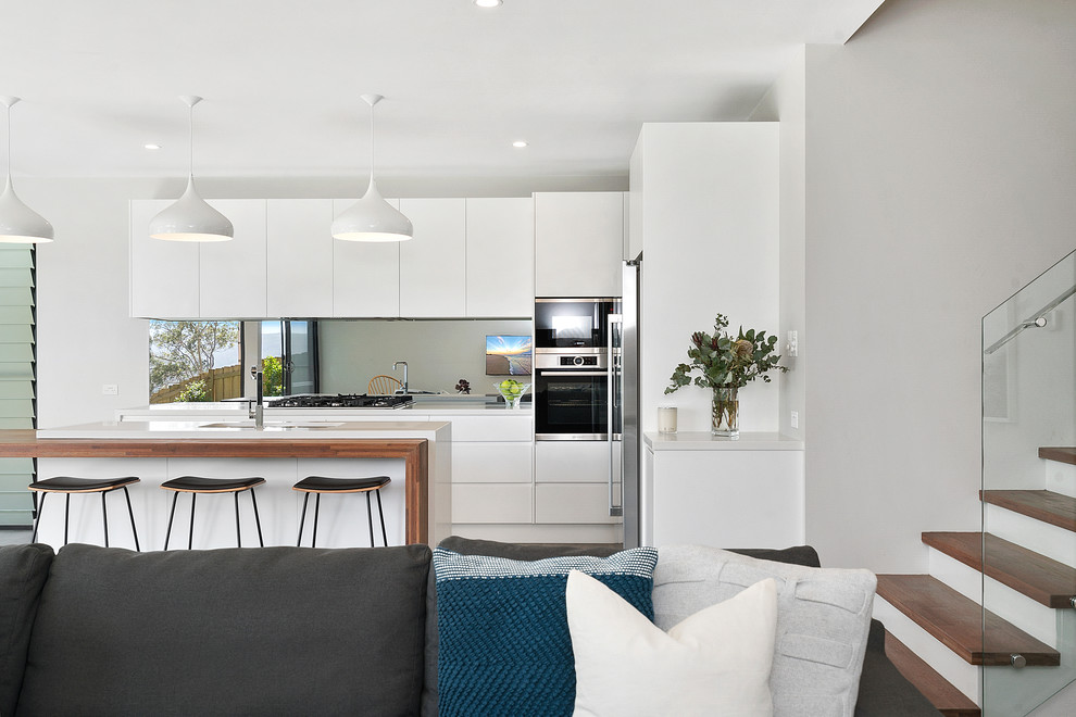 Design ideas for a large modern galley kitchen in Sunshine Coast with a double-bowl sink, recessed-panel cabinets, white cabinets, wood benchtops, grey splashback, mirror splashback, stainless steel appliances, light hardwood floors, with island, grey floor and white benchtop.
