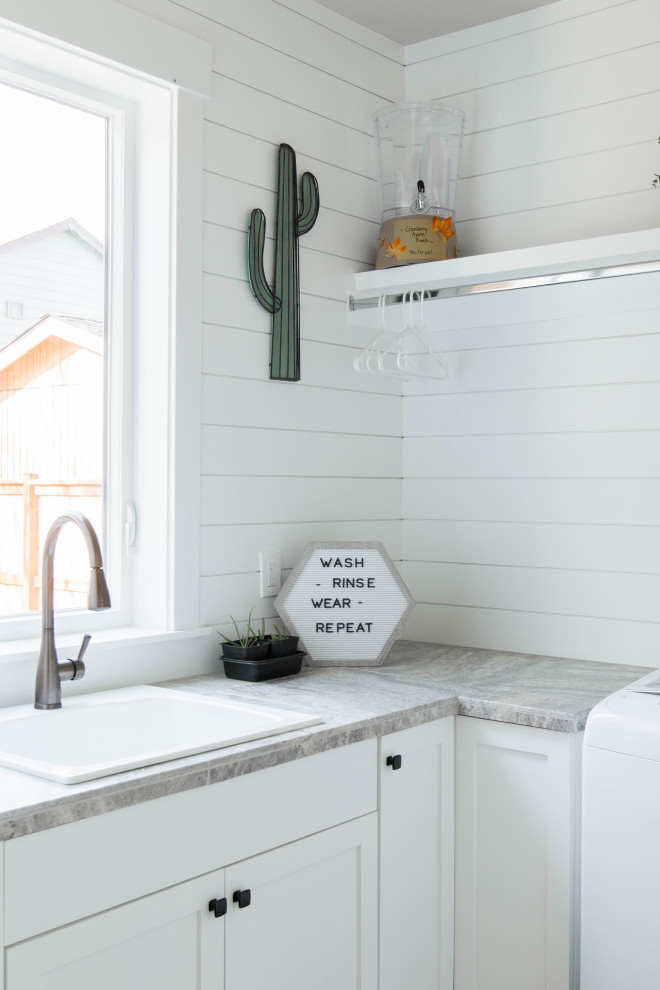 Inspiration for a mid-sized arts and crafts l-shaped dedicated laundry room in Portland with a drop-in sink, recessed-panel cabinets, white cabinets, limestone benchtops, white walls, a side-by-side washer and dryer and grey benchtop.
