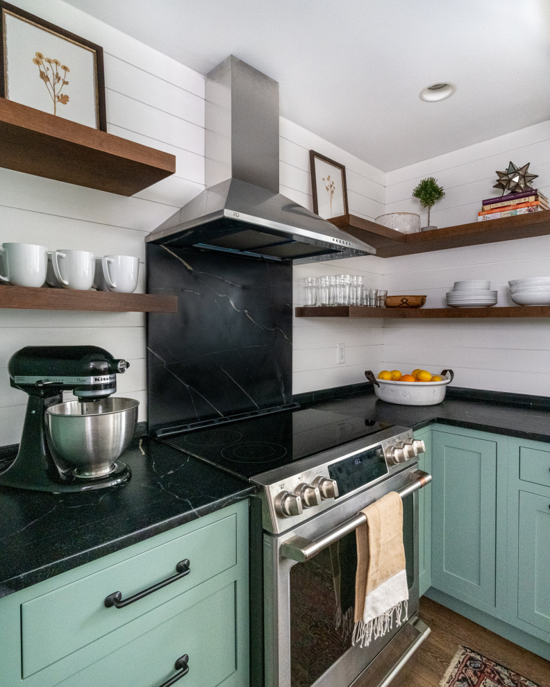 Example of a small cottage l-shaped laminate floor and brown floor enclosed kitchen design in Philadelphia with a farmhouse sink, shaker cabinets, green cabinets, soapstone countertops, black backsplash, stone slab backsplash, stainless steel appliances, an island and black countertops