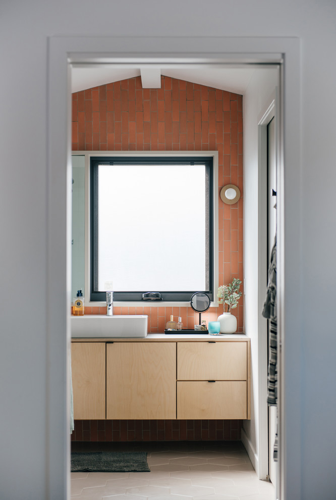 Small midcentury master bathroom in Orange County with furniture-like cabinets, light wood cabinets, pink tile, ceramic tile, pink walls, porcelain floors, a vessel sink, wood benchtops, beige floor and grey benchtops.