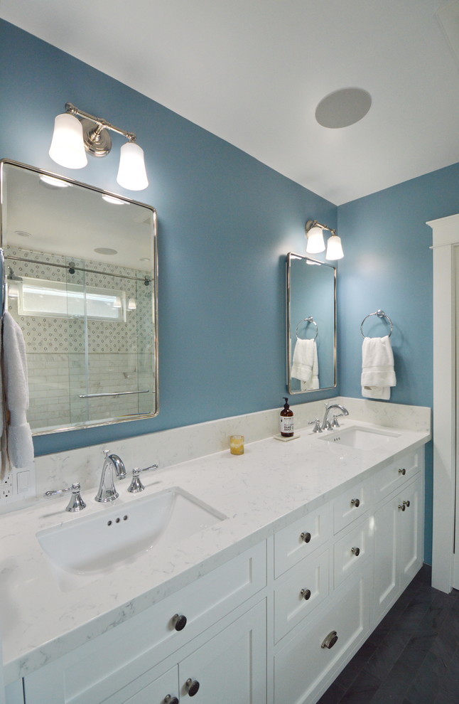 Photo of an arts and crafts master bathroom in Los Angeles with recessed-panel cabinets, medium wood cabinets, a corner tub, a corner shower, a two-piece toilet, white tile, white walls, laminate floors, an undermount sink, engineered quartz benchtops, grey floor, a sliding shower screen and white benchtops.