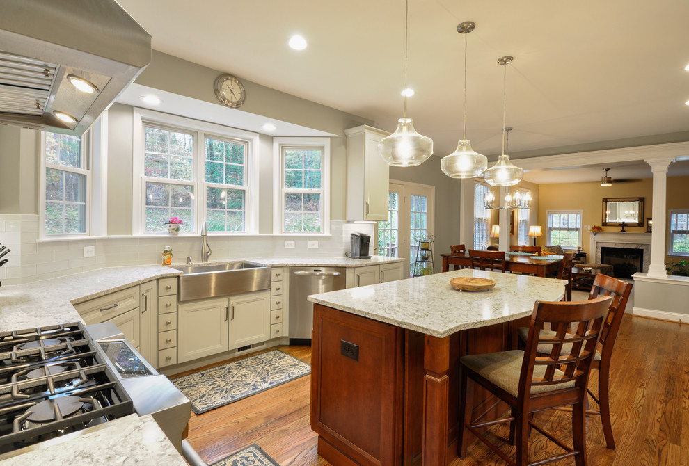This is an example of a large transitional u-shaped kitchen in DC Metro with a farmhouse sink, recessed-panel cabinets, quartz benchtops, white splashback, stainless steel appliances, medium hardwood floors and with island.