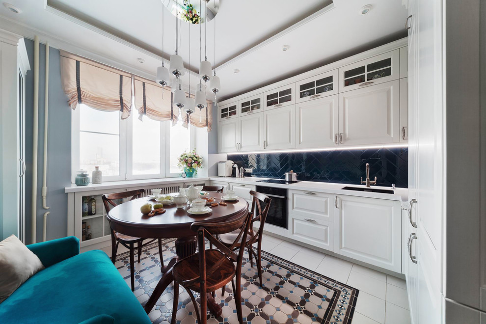 This is an example of a transitional l-shaped eat-in kitchen in Yekaterinburg with raised-panel cabinets, white cabinets, solid surface benchtops, blue splashback, white benchtop, an undermount sink, glass tile splashback and porcelain floors.