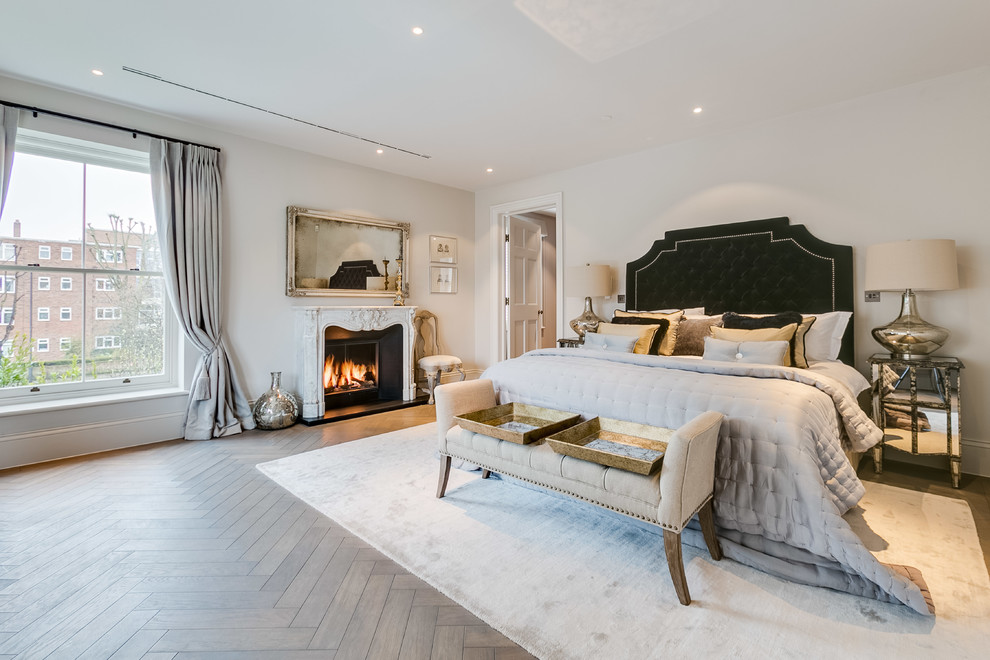 Large traditional master bedroom in London with white walls, light hardwood floors, a standard fireplace and beige floor.