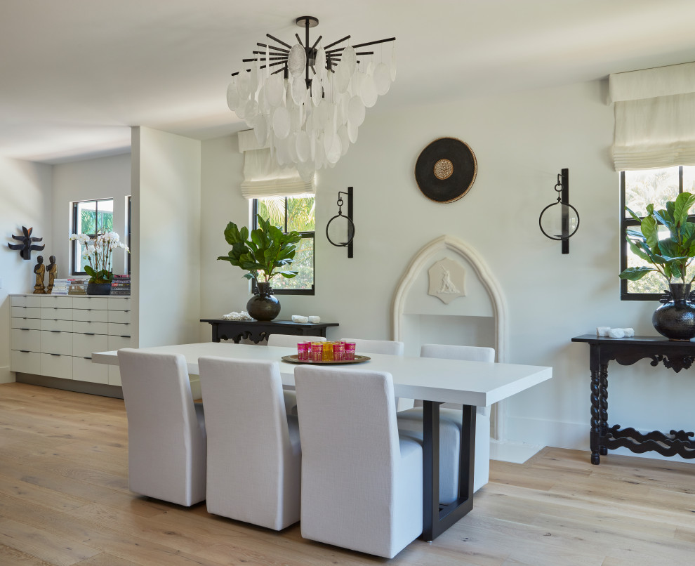 Photo of a mid-sized transitional separate dining room in Miami with white walls, light hardwood floors, a standard fireplace and a plaster fireplace surround.