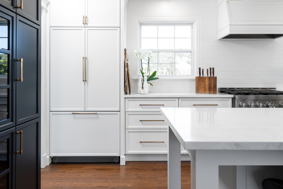 Inspiration för mellanstora moderna vitt l-kök, med en undermonterad diskho, luckor med infälld panel, vita skåp, bänkskiva i koppar, vitt stänkskydd, stänkskydd i keramik, integrerade vitvaror, mellanmörkt trägolv, en köksö och brunt golv
