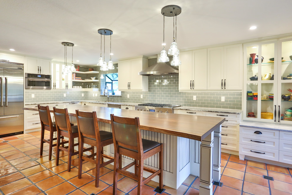 Large traditional galley eat-in kitchen in Austin with a single-bowl sink, shaker cabinets, yellow cabinets, wood benchtops, green splashback, glass tile splashback, white appliances, travertine floors, with island and brown benchtop.